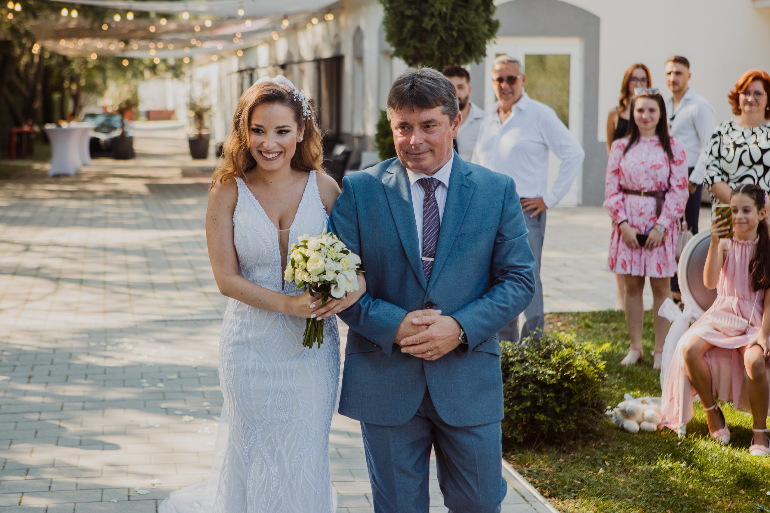 A menyasszony bevonulása a polgári szertartásra az örömapával, mind a ketten mosolyognak.