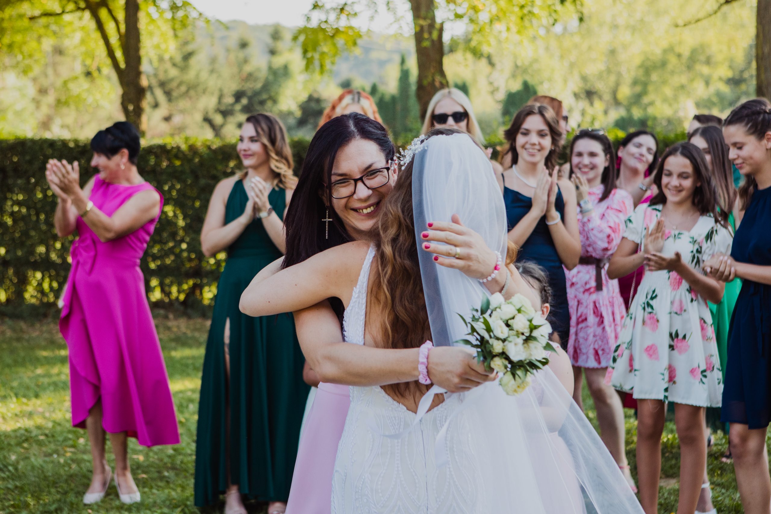 A fekete hajú hölgy elkapta a menyasszonyi csokrot és ölelkezve gratulálnak egymásnak.